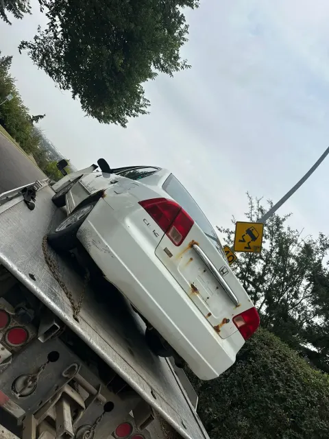 Rusted white Honda Civic loaded on a flatbed tow truck for scrap car removal